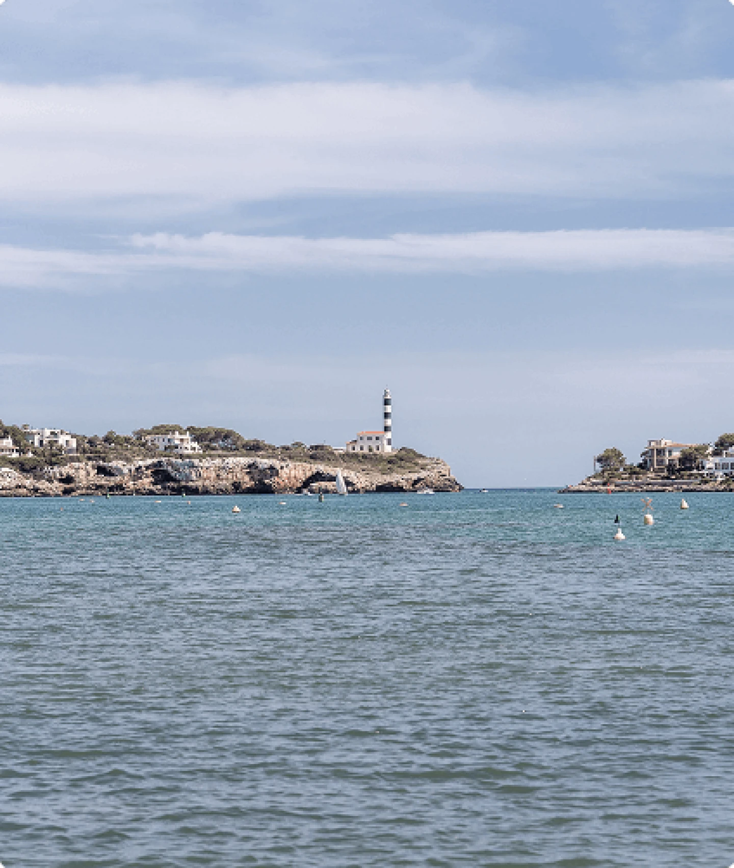 View of the iconic striped lighthouse and calm waters of the Porto Colom harbour